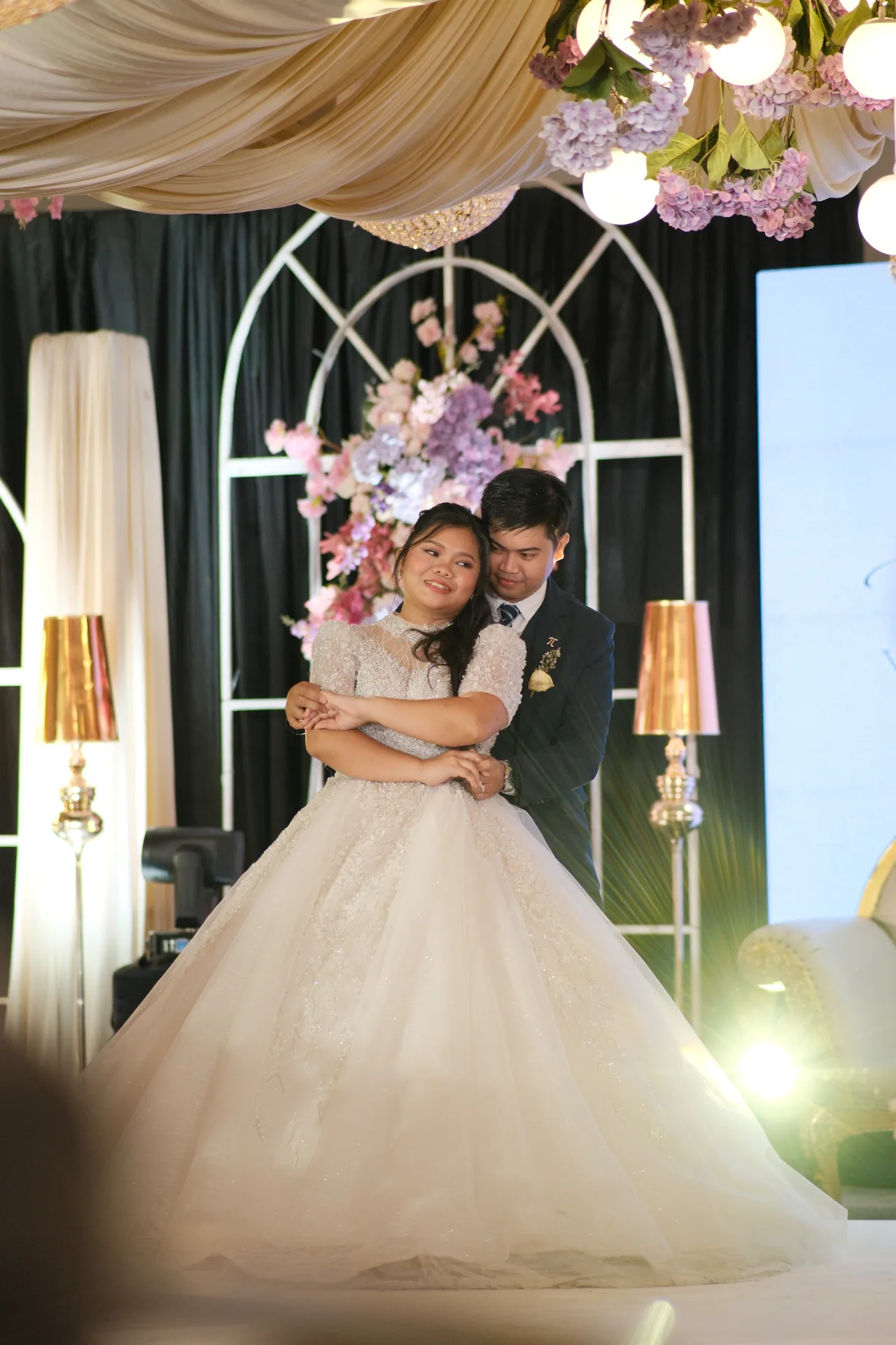 Webster and Krystelle in a quiet embrace under the floral arch at the reception.