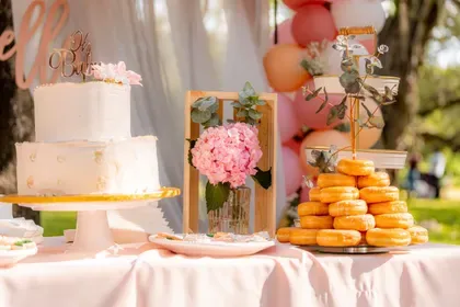 An outdoor garden dessert table with a soft white cake, pink hydrangeas and a donut tower.