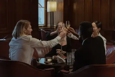 Colleagues in formal attire clink champagne flutes in a warm wood-panelled lounge.
