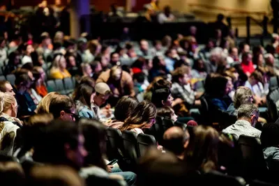 A packed crowd of attendees seated in a warmly lit auditorium during a live event.